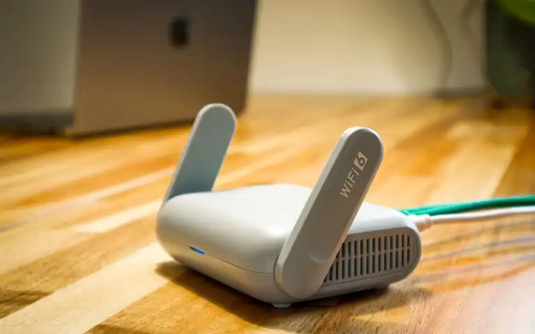 A Wi-Fi router with antennas and cable sits on a wooden desk.