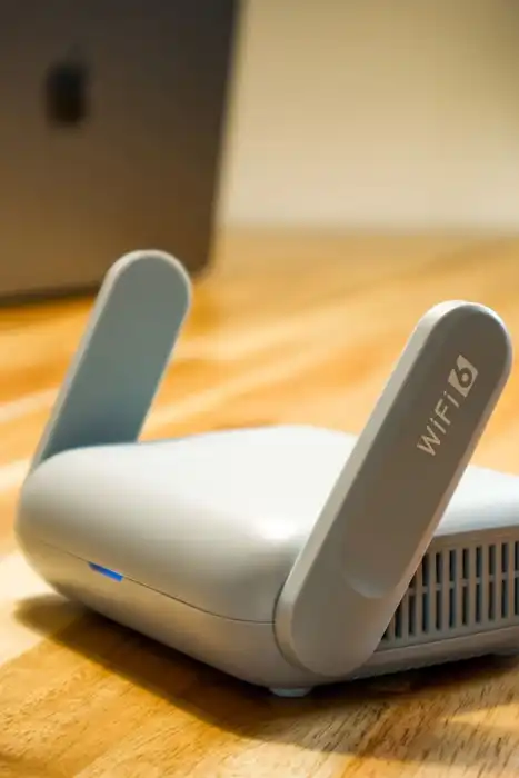 A Wi-Fi router with antennas and cable sits on a wooden desk.