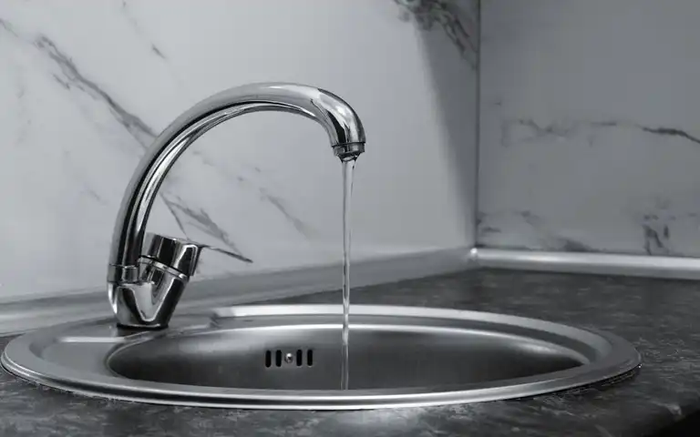 Chrome kitchen faucet running into a stainless-steel sink.