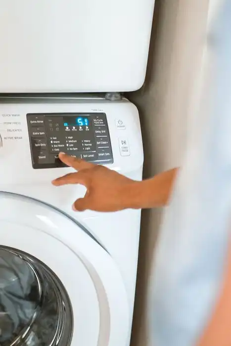A hand selects a cycle on a front-loading washing machine control panel.