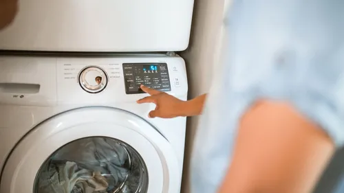 A hand selects a cycle on a front-loading washing machine control panel.