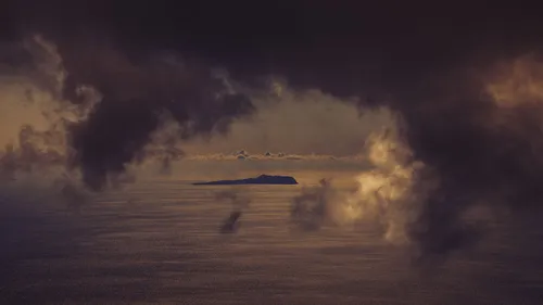 Storm clouds hang over a distant island and dark ocean beneath a band of cloud near the horizon.