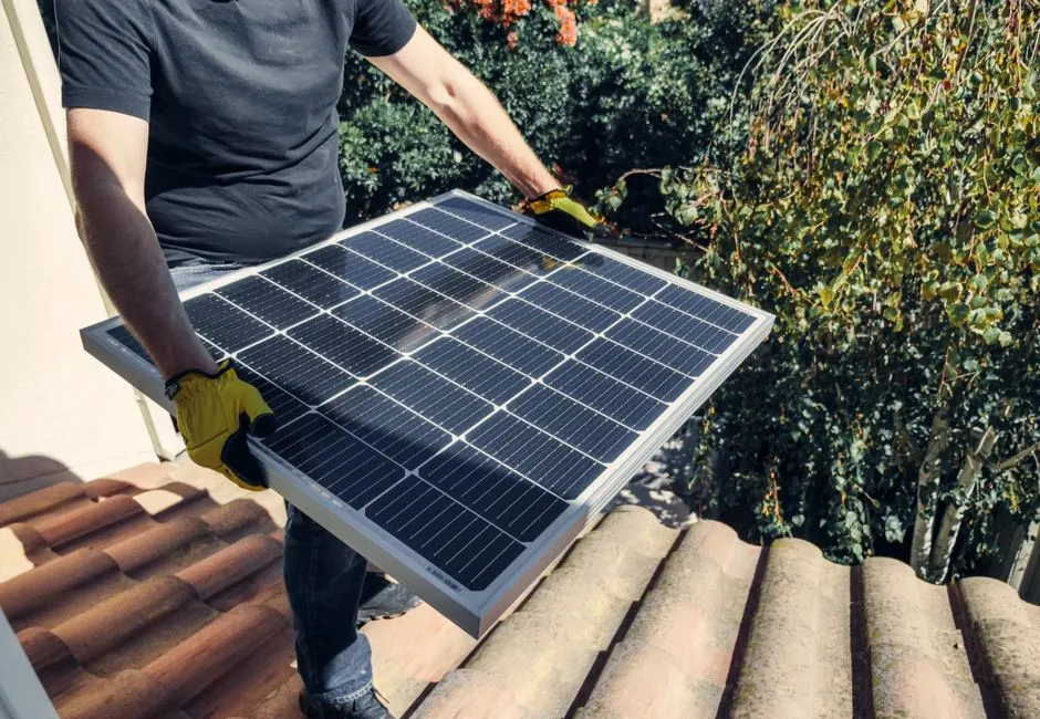 Worker positioning a solar panel on a residential roof