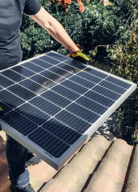 Worker positioning a solar panel on a residential roof