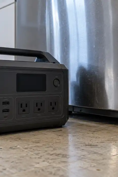 An unplugged portable battery station on a kitchen floor beside a refrigerator