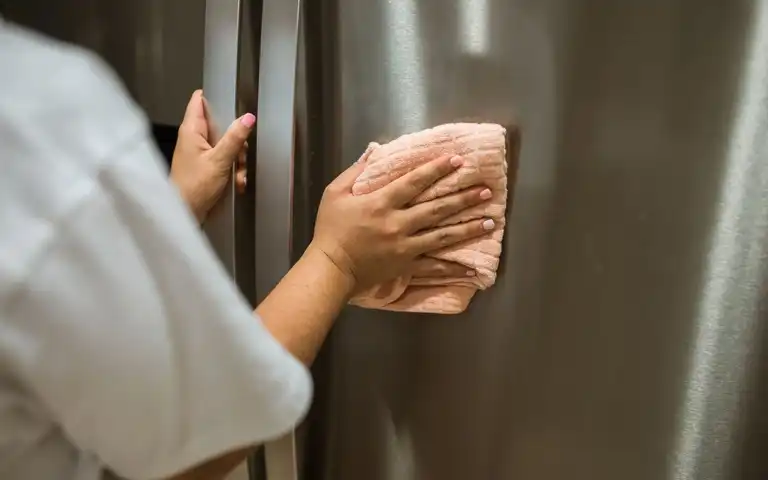 A person wipes the stainless-steel exterior of a refrigerator.