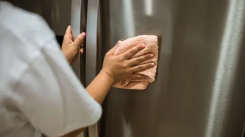 A person wipes the stainless-steel exterior of a refrigerator.