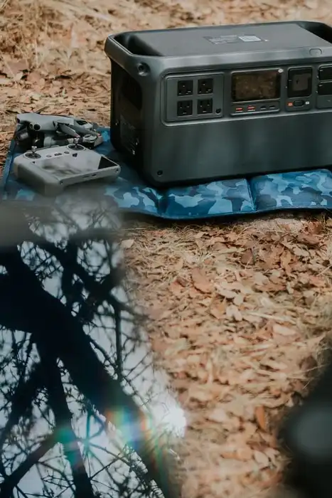 A portable power station sits on a patterned mat among leaves outdoors.