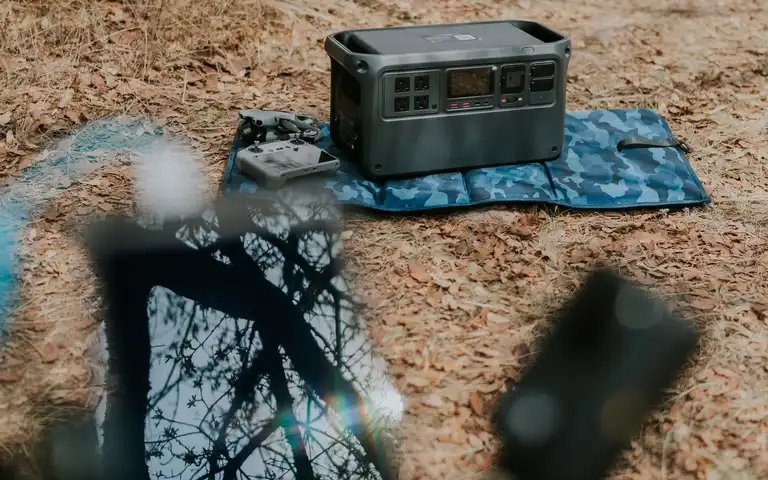 A portable power station sits on a patterned mat among leaves outdoors.