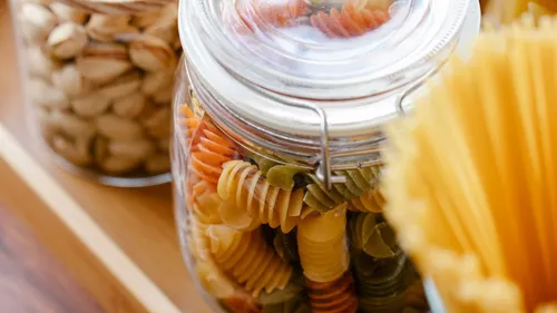 Glass jars containing dry spiral pasta and other pantry ingredients on a wooden tray.