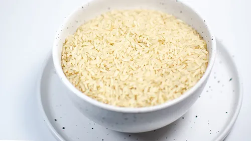 Uncooked rice grains in a speckled white bowl on a matching plate.