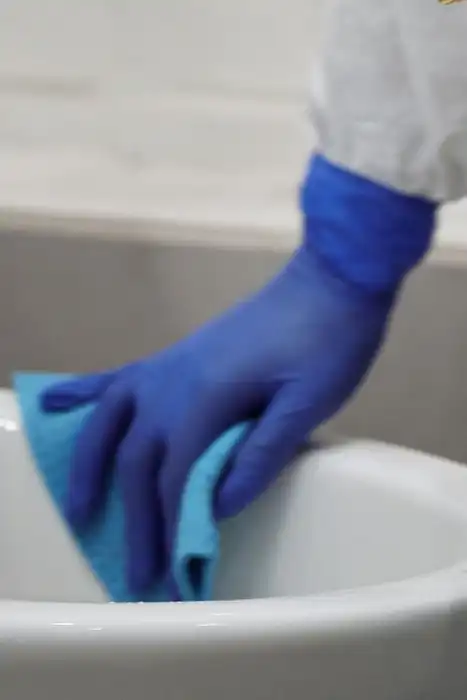 A person in protective gear cleaning a toilet in a bathroom.