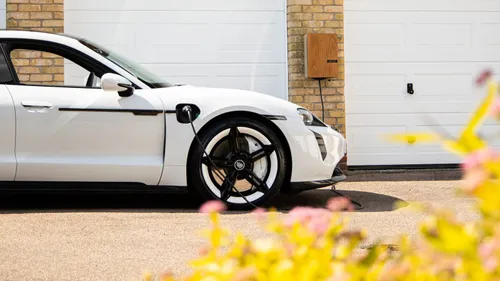White electric car connected to a wall-mounted charger beside a garage.
