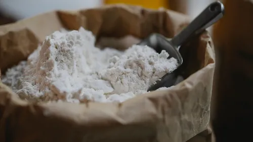 A metal scoop rests in flour inside an open paper bag.