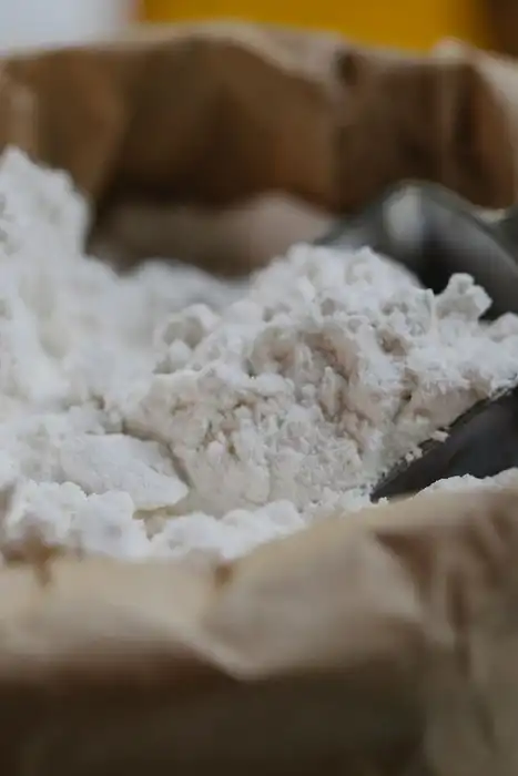 A metal scoop rests in flour inside an open paper bag.