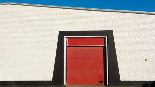 A closed red garage door fills the center of a white brick building.