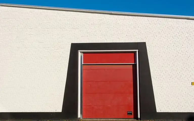 A closed red garage door fills the center of a white brick building.