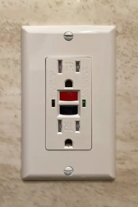 A white North American GFCI receptacle with red reset and black test buttons.