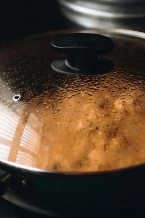 Steam beads on the glass lid of a pan sitting on a stovetop.