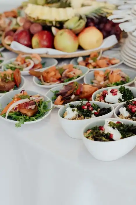 Small dishes of prepared food and fruit are arranged on a buffet table.