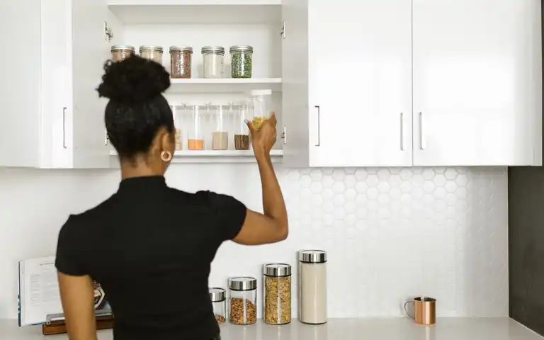 A person placing a jar on a shelf in a bright kitchen pantry