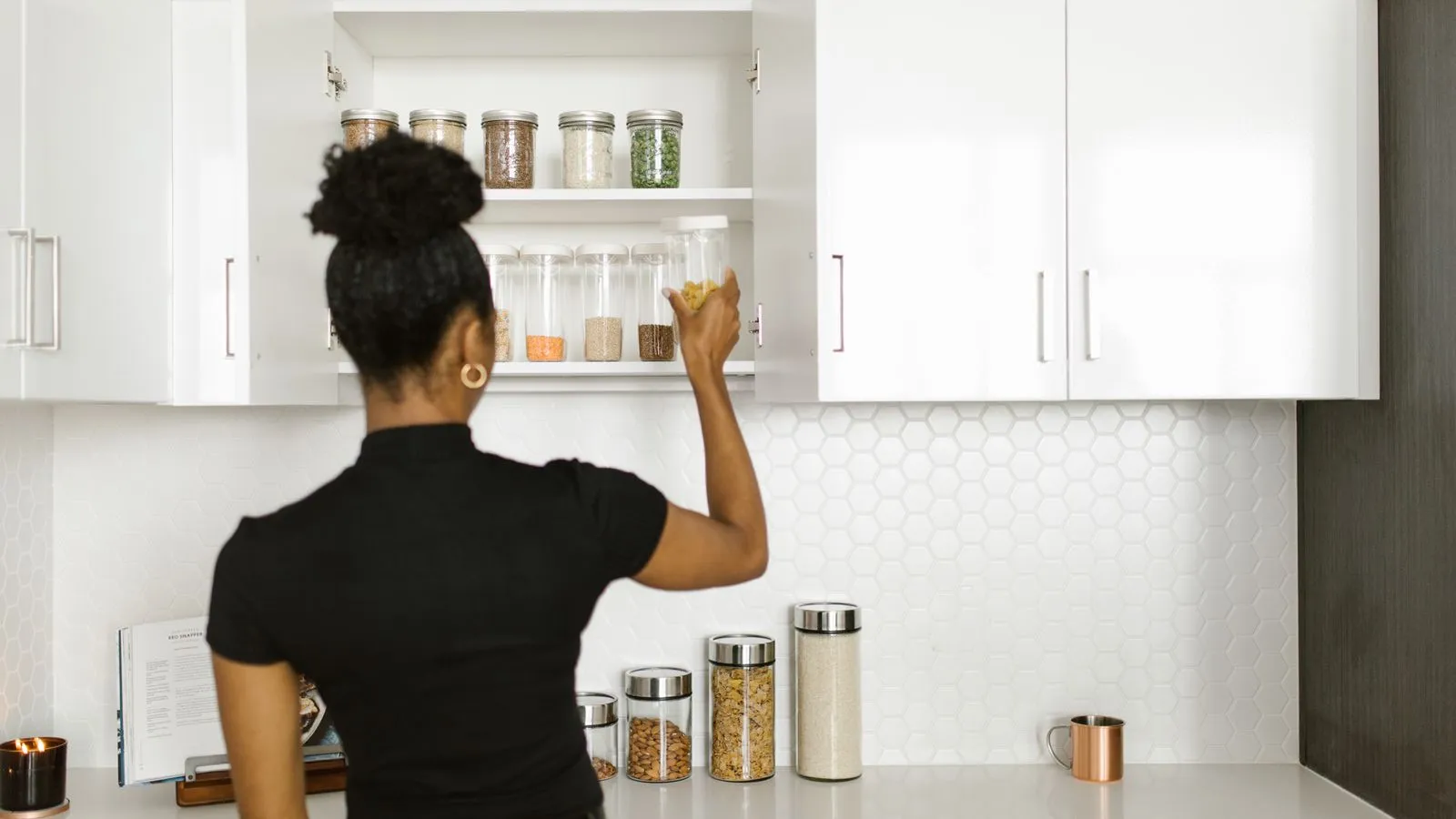 A person placing a jar on a shelf in a bright kitchen pantry