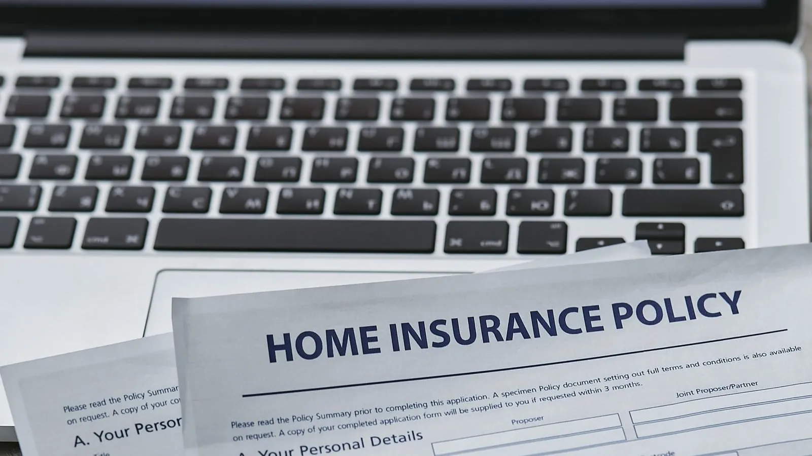 Home insurance paperwork beside a laptop and keyboard.