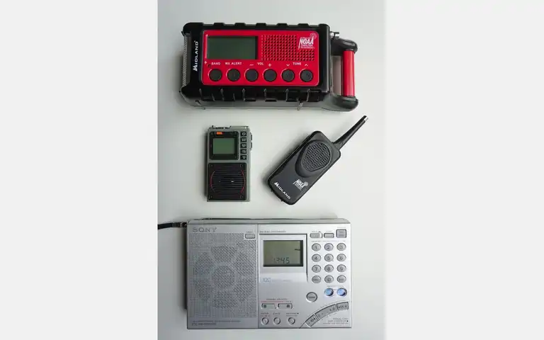 Several portable radios arranged on a light surface, including a red weather-alert receiver and handheld units.