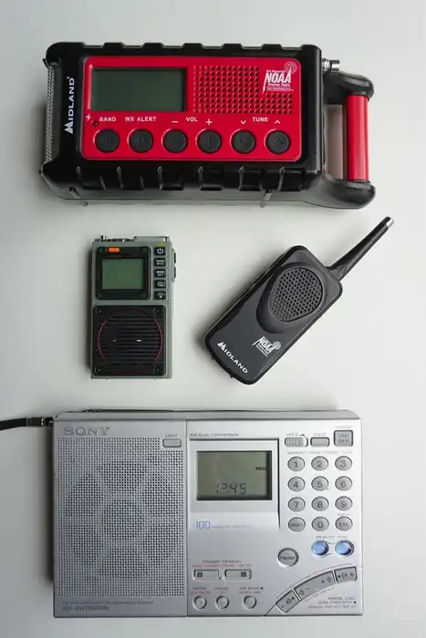 Several portable radios arranged on a light surface, including a red weather-alert receiver and handheld units.