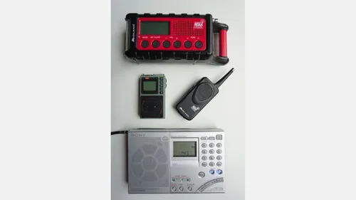 Several portable radios arranged on a light surface, including a red weather-alert receiver and handheld units.
