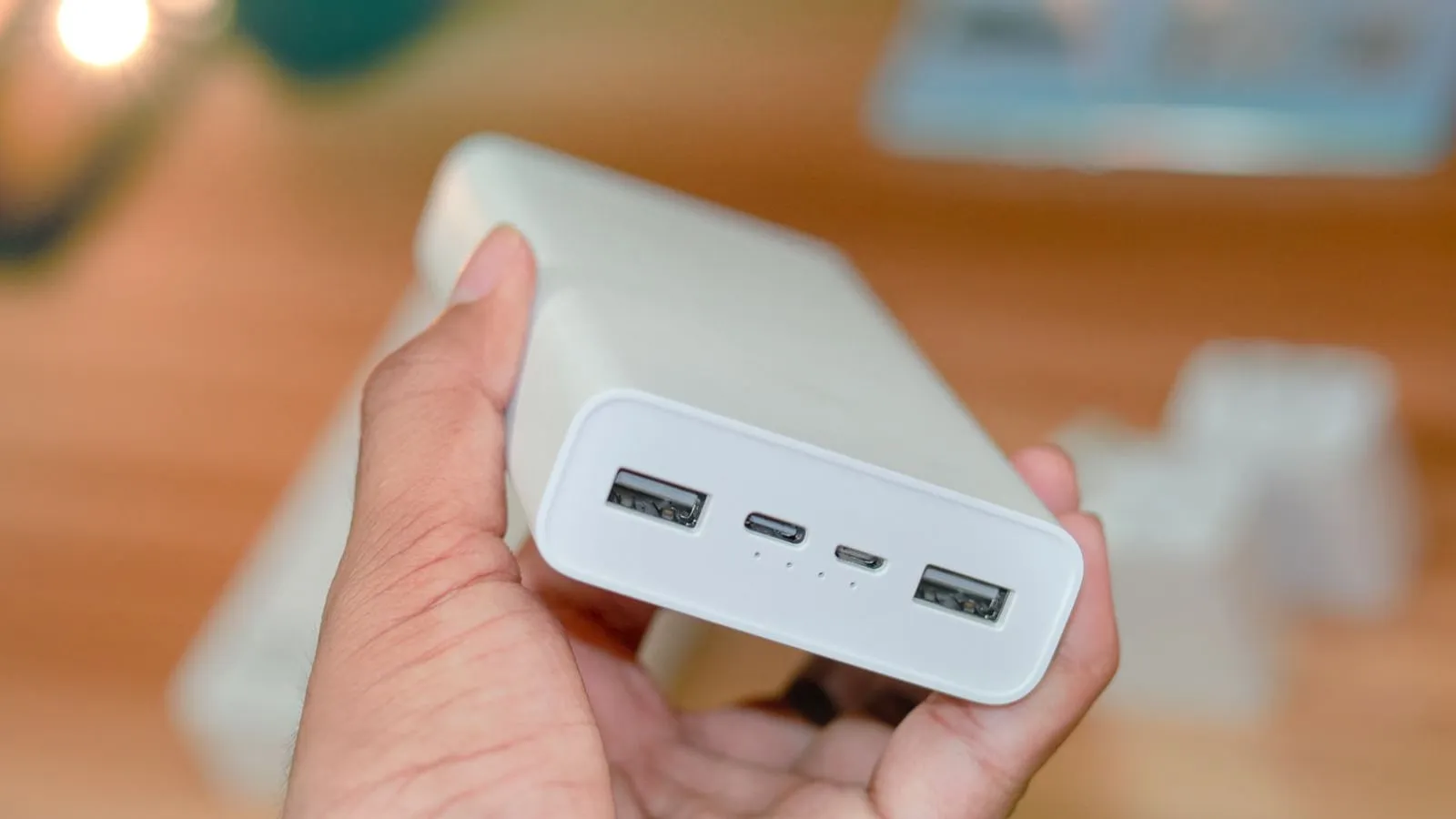A hand holds a white power bank with several charging ports visible.