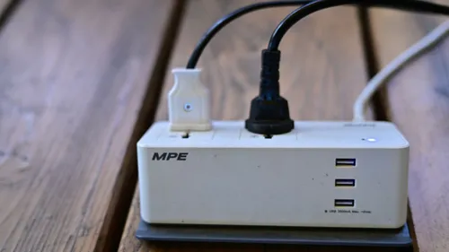 Power strip with two connected plugs and three USB ports on a wooden surface.
