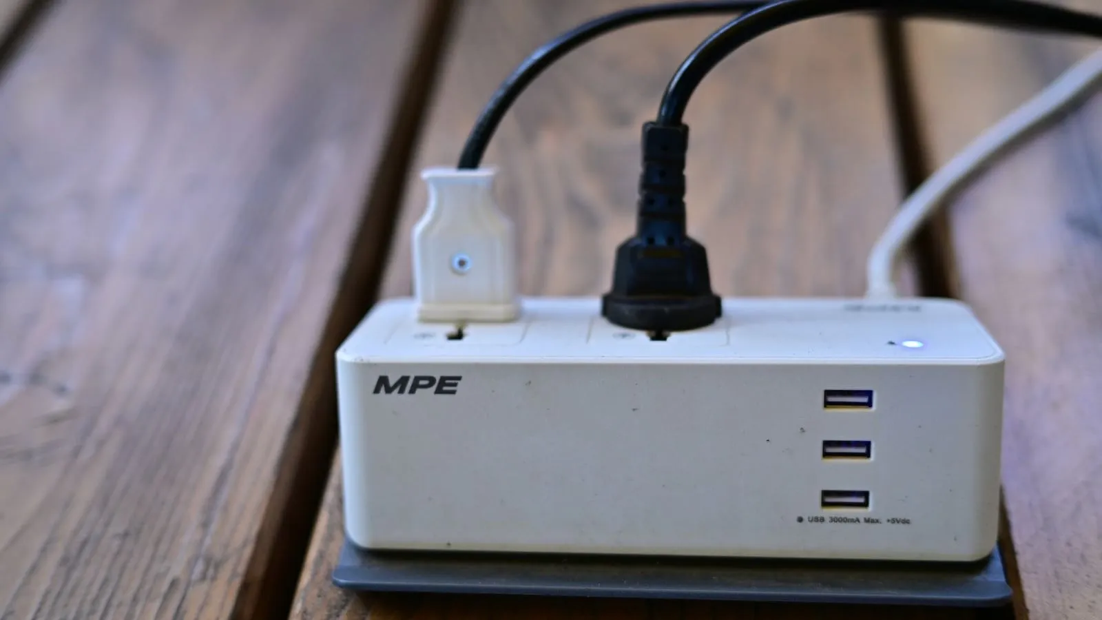 Power strip with two connected plugs and three USB ports on a wooden surface.