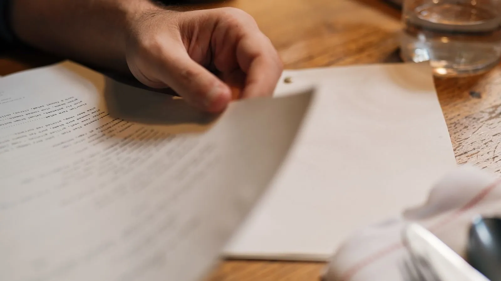 A hand resting on a printed document beside a glass of water.