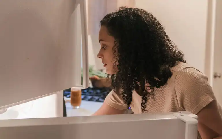 A woman checks the contents of an open refrigerator.