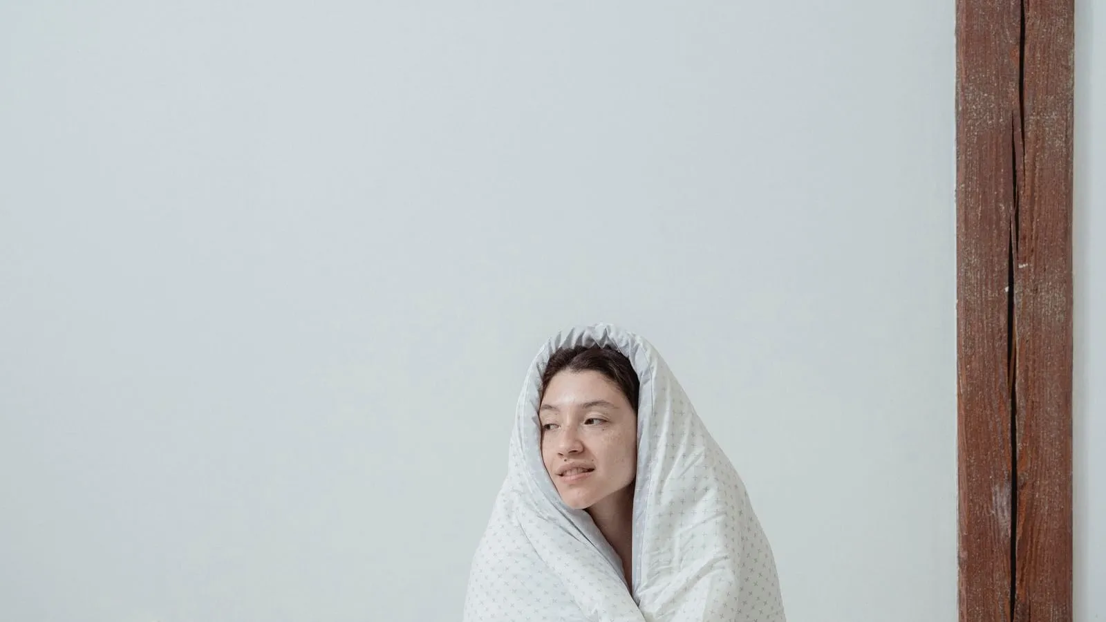 A person wrapped in a light blanket while sitting on a bed.