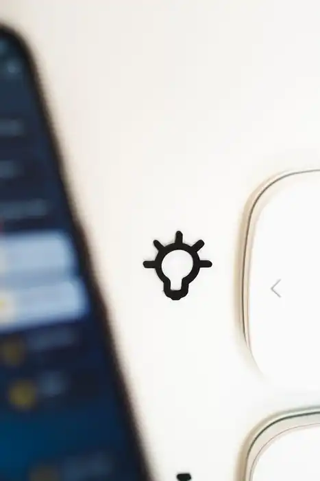 A hand holds a smartphone beside two smart-home wall controls.