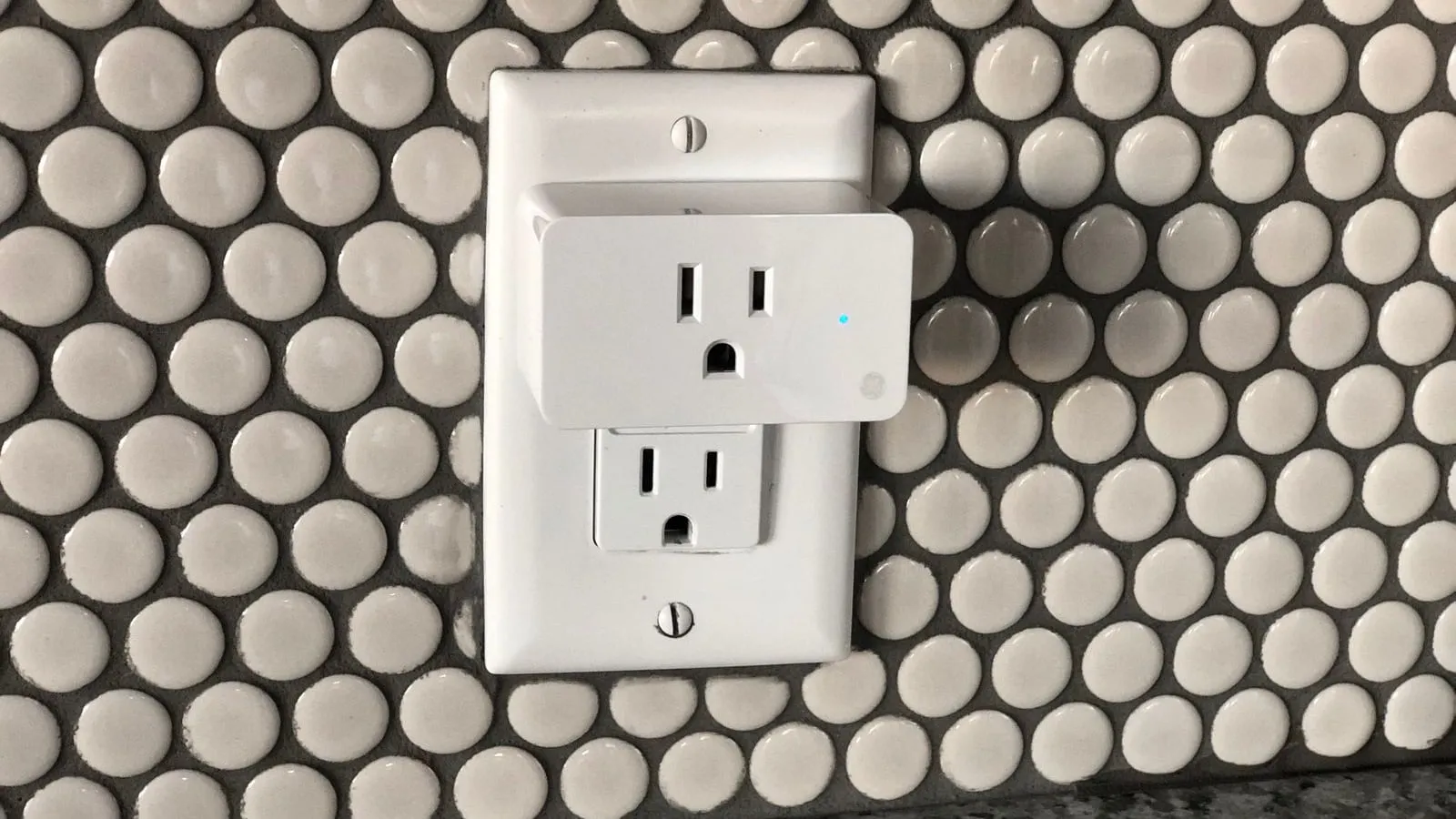A white plug-in outlet adapter against a wall of circular tiles.