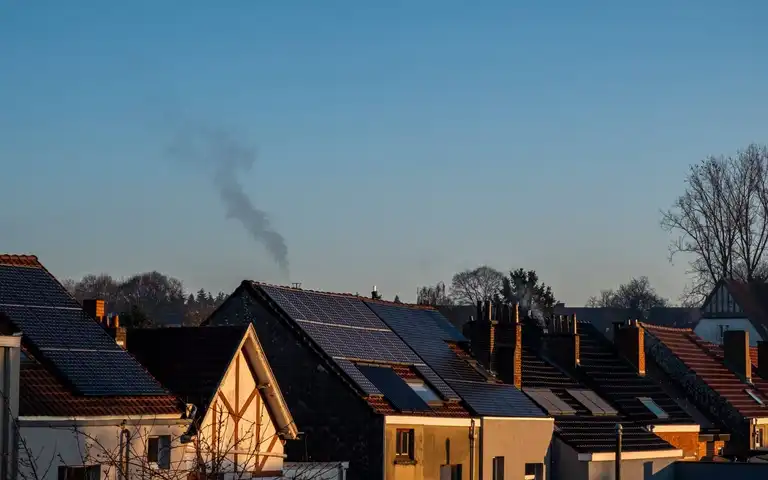 Solar panels on the roofs of neighboring houses under a clear sky.
