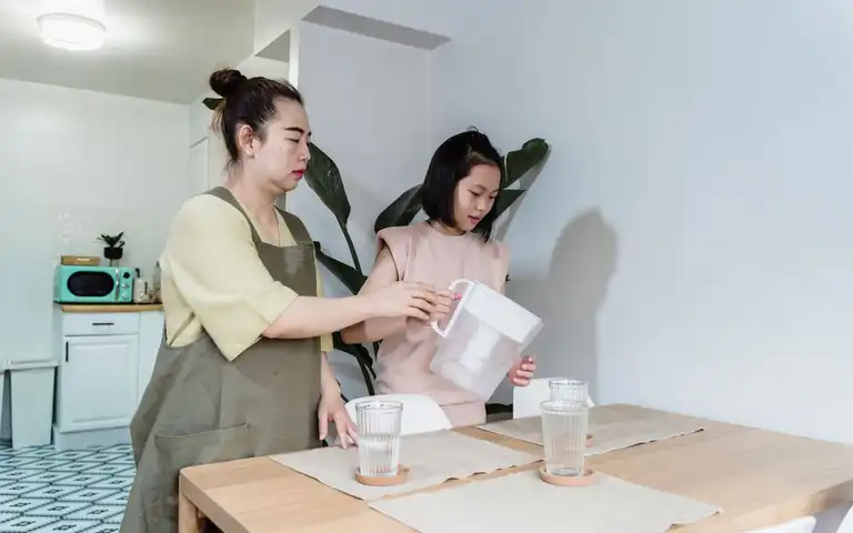 A woman and child pour water from a filter jug at a kitchen table.