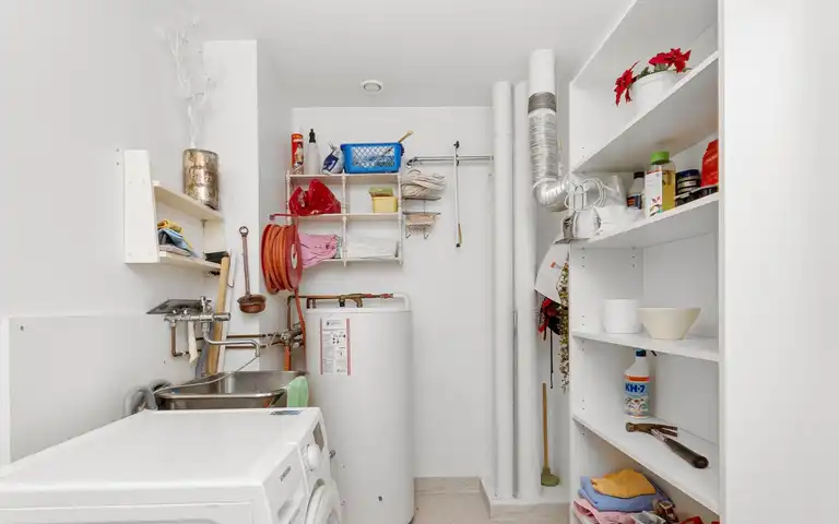 A storage water heater beside a washer and utility sink in a laundry room.