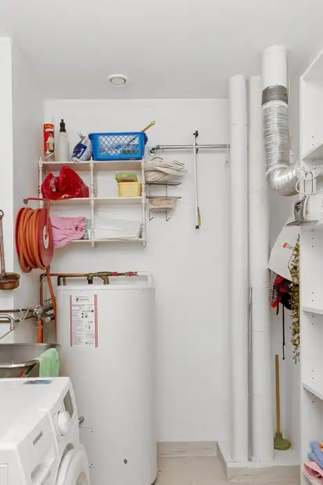 A storage water heater beside a washer and utility sink in a laundry room.