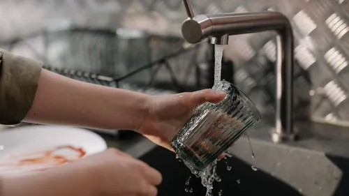 A hand rinses a drinking glass under a kitchen faucet.