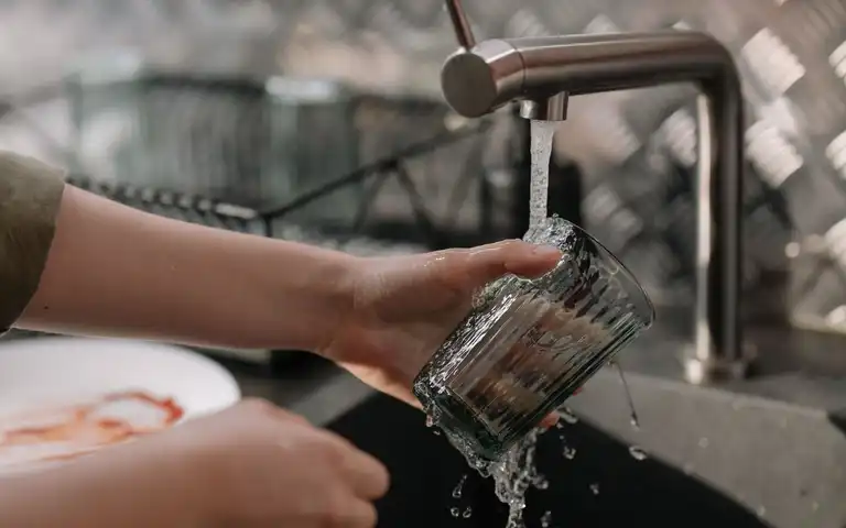 A hand rinses a drinking glass under a kitchen faucet.