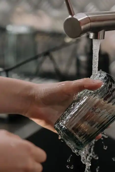 A hand rinses a drinking glass under a kitchen faucet.