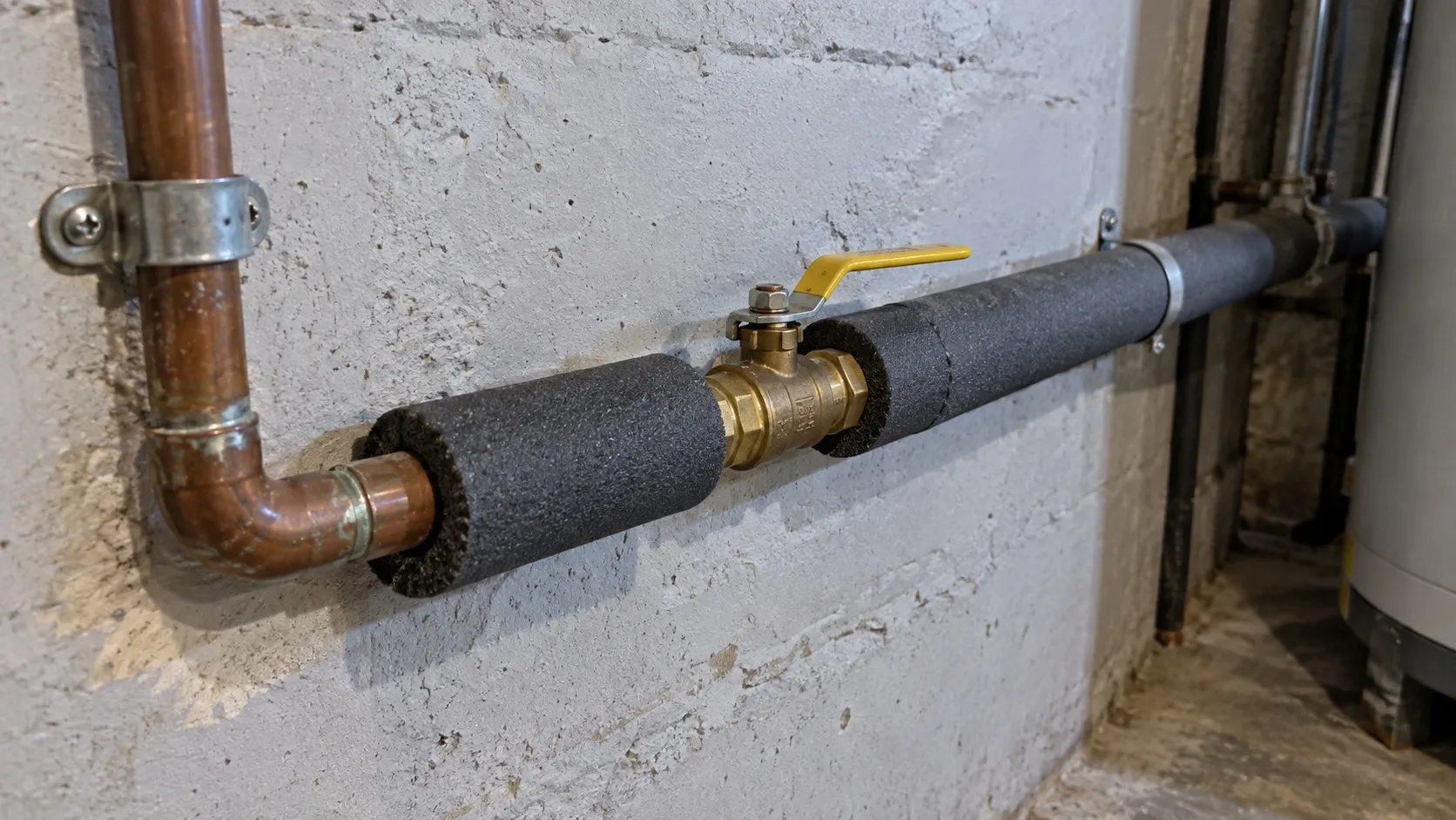 Foam insulation around a basement pipe with an accessible brass shutoff valve